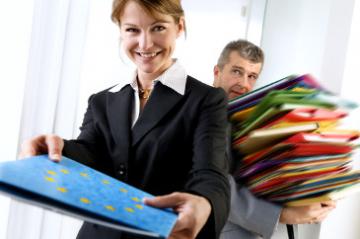 A woman holding a folder with the EU emblem while a man holds a pile of other folders in the background © EU