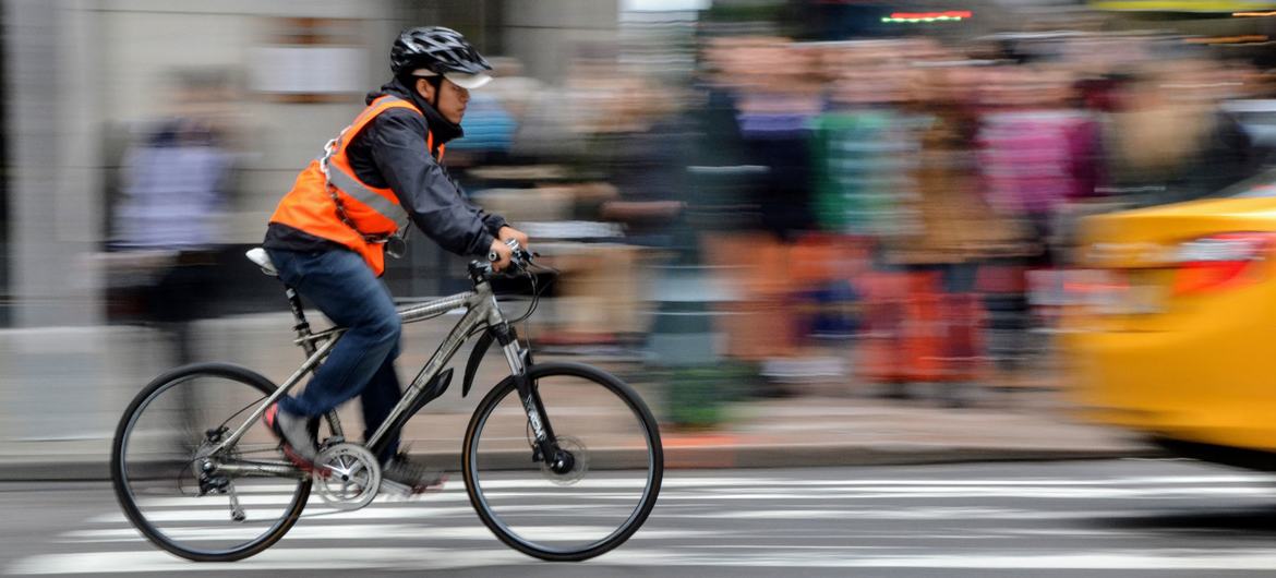A man wears a helmet and reflective vest while cycling in Manhattan, New York.