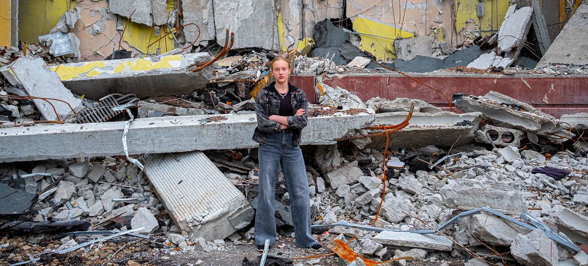 A twelve-year-old girl stands in front of her school in Kharkiv, Ukraine. It was destroyed in an air strike and she will now study online.