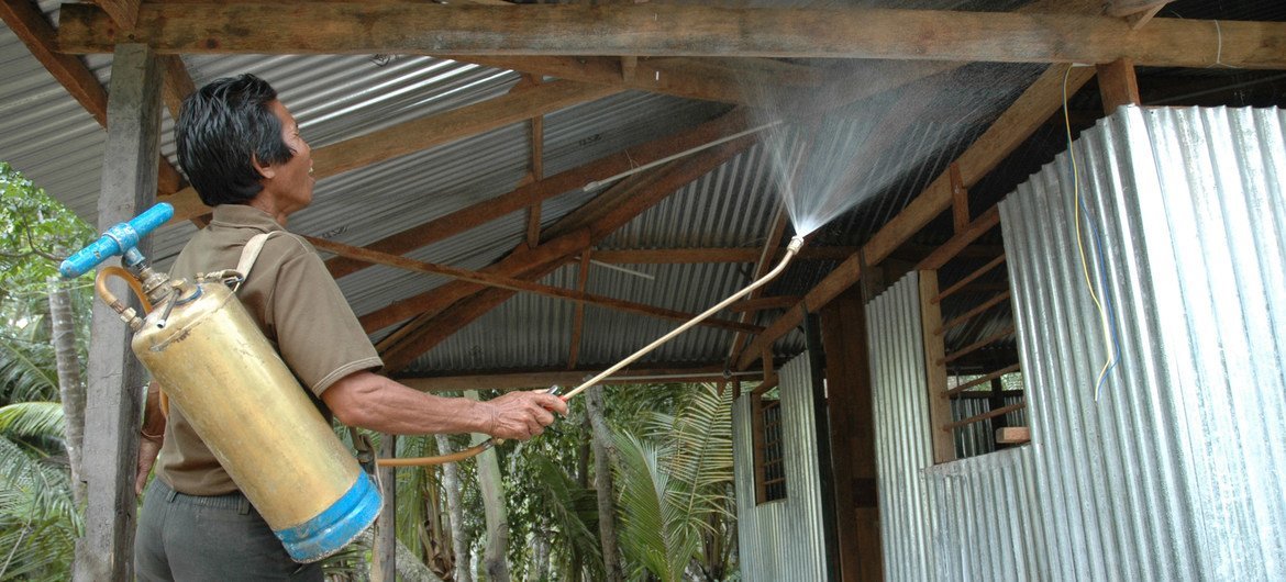 A worker sprays insecticide on the surfaces of a shelter to control the spread of mosquitoes and mitigate the risk of malaria.
